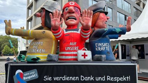 Drei Figuren auf einem Wagen stellen einen Feuerwehrmann, einen Sanitäter und einen Polizisten dar. Darunter steht: "Sie verdienen Dank und Respekt"